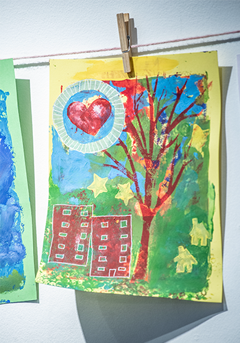 Print of a heart, tree and multi-storey building. Print is hanging on a string held by a clothes peg.
