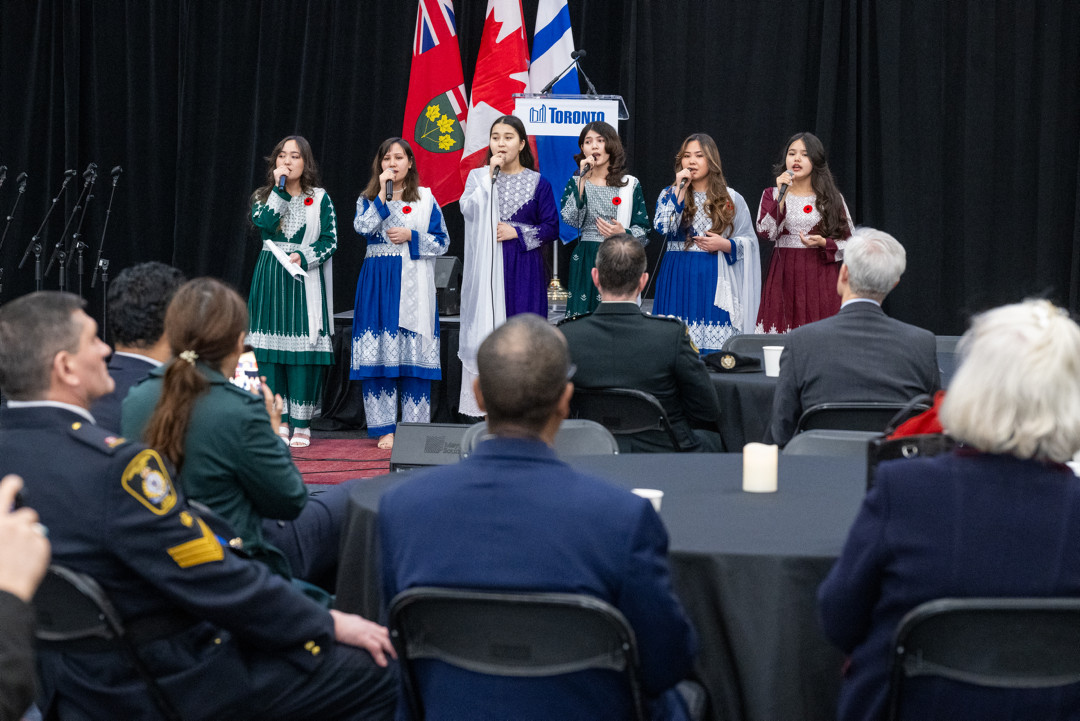 Six girls in traditional dress perform in front of an audience