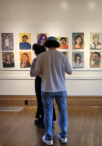 Two people standing in a gallery room in front of portraits on the wall