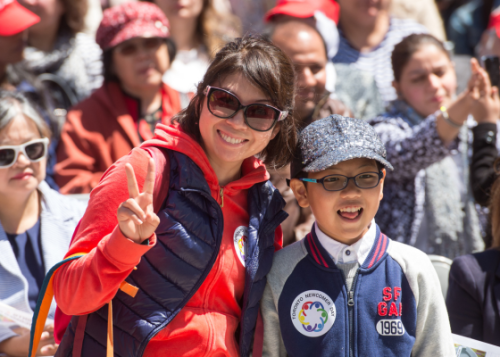 Adult giving a peace sign and child look to camera and crowd of people in background
