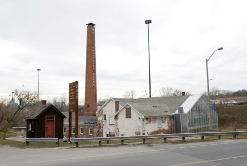Image depicts colour photograph of Victorian industrial buildings with modern glass addition, with chimney in background