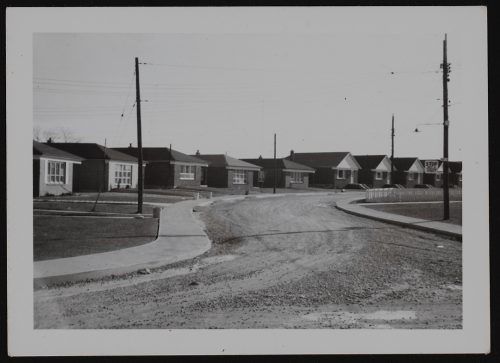 Image depicts monochrome photograph of newly built bungalow houses and unfinished thorougfare