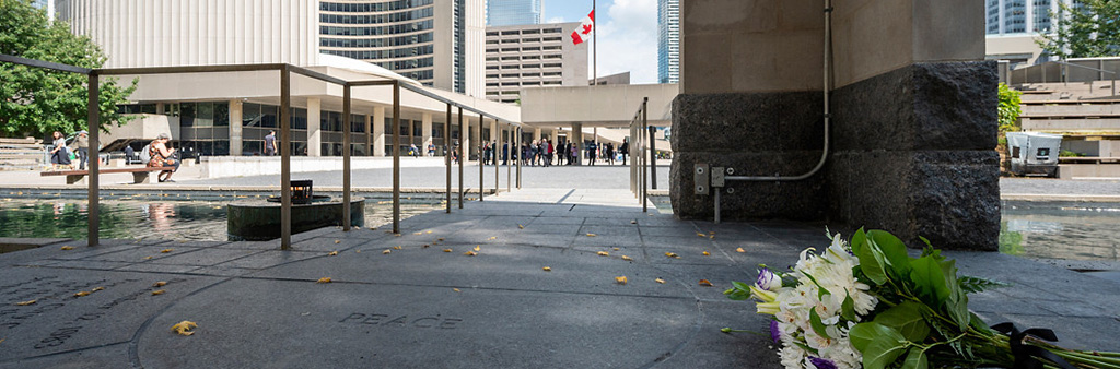 A bouquet of flowers placed on a commemorative tile reading "Peace" in the Peace Garden in Nathan Phillips Square outside Toronto City Hall.