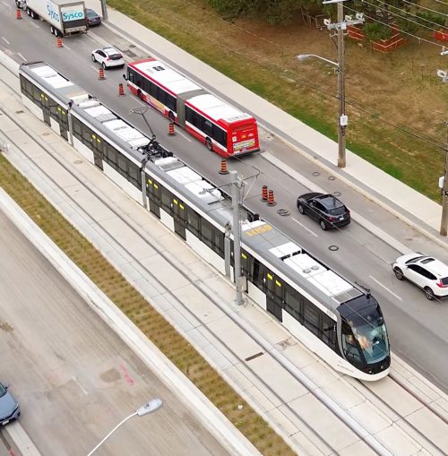 A Light Rail Transit vehicle stationed on tracks between lanes of traffic. 