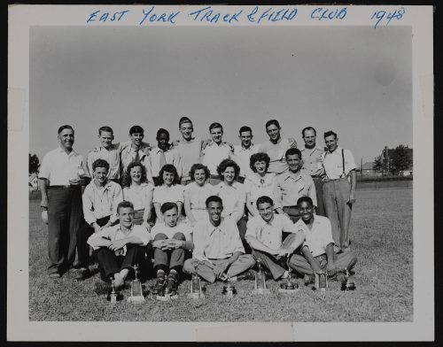 Image depicts monochrome photograph of group portrait of athletes with trophies