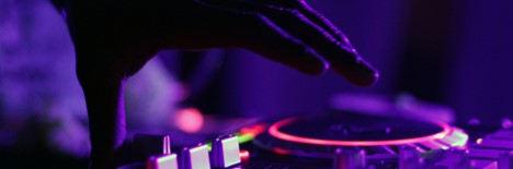 A hand is shown over a mixing device used by a DJ in a nightclub setting.