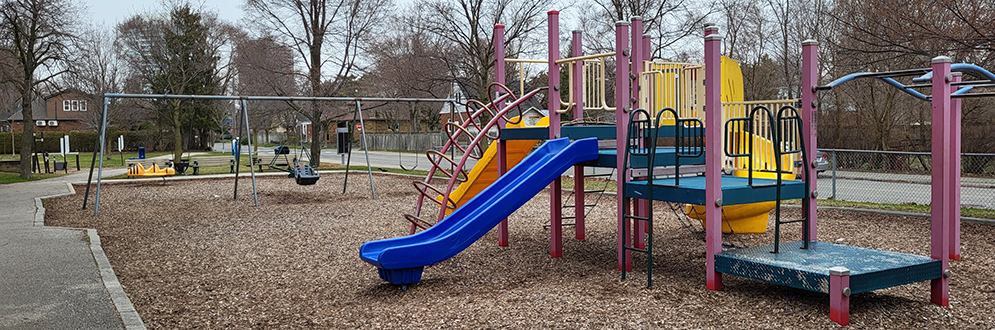 Denison Park Playground with a ply structure with a blue slide in the foreground and a swing set in the background.