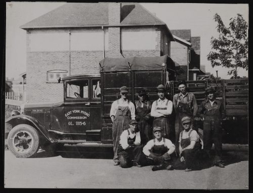 Image depicts monochrome photograph of workmen next to truck