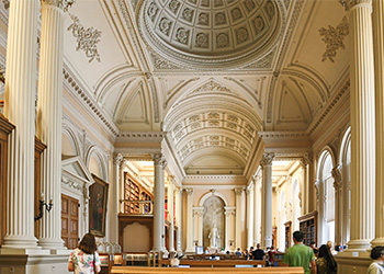 People walking through an ornate neo-classical room with Corinthian columns, vaulted ceiling and a niche with a sculpture