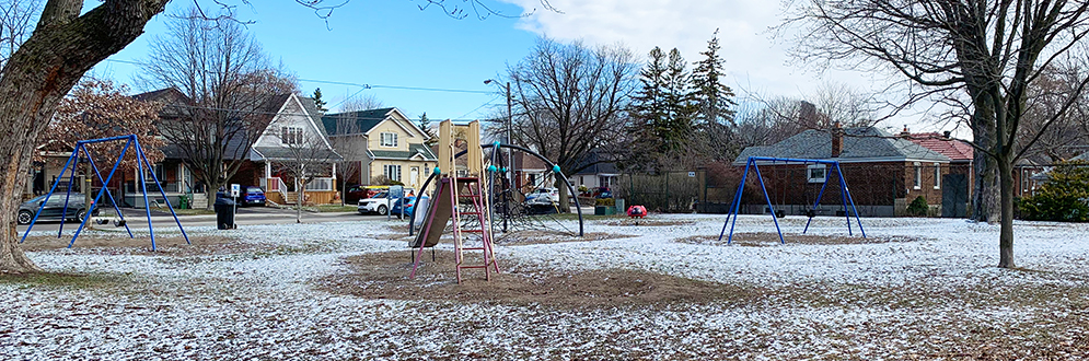 Hillside Park Playground in the winter showing a standalone slide and curved climbing structure in the middle and a swing set on either side.