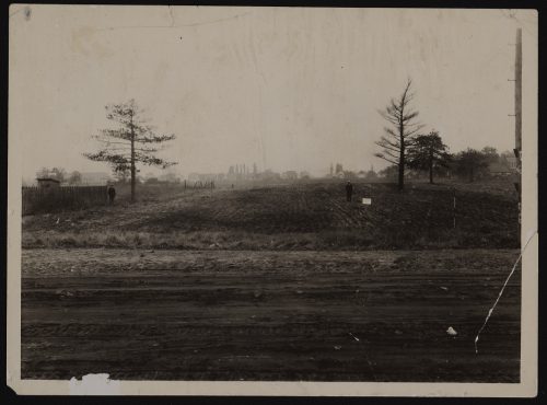 Image depicts monochrome photograph of street in foreground with farmland in background