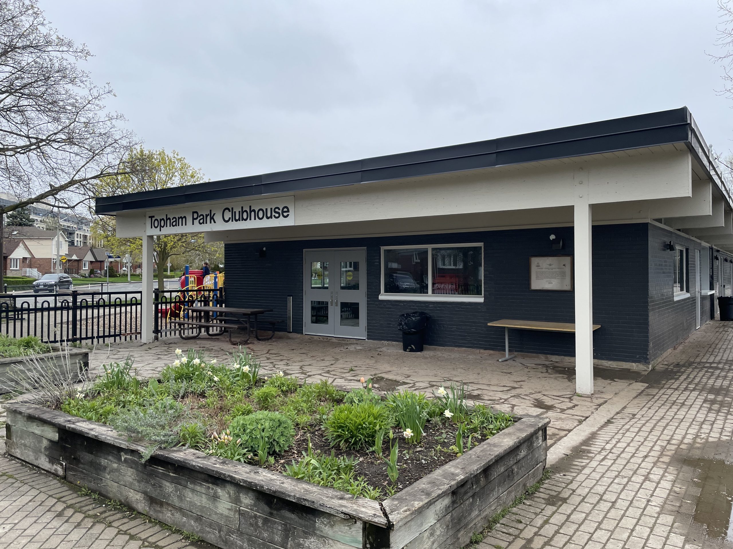 Exterior of the clubhouse, which is dark blue, with a flower bed in the foreground.