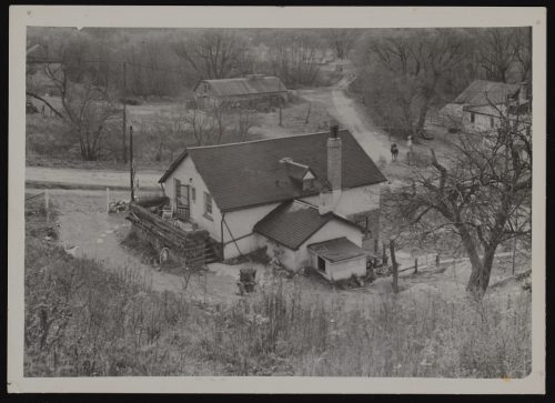 Image depicts monochrome photograph of Victorian industrial buildings in amongst mature trees