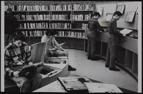 Image depicts monochrome photograph of young people listening to records in a library