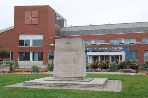 Image depicts colour photograph of municipal building with war memorial in foreground