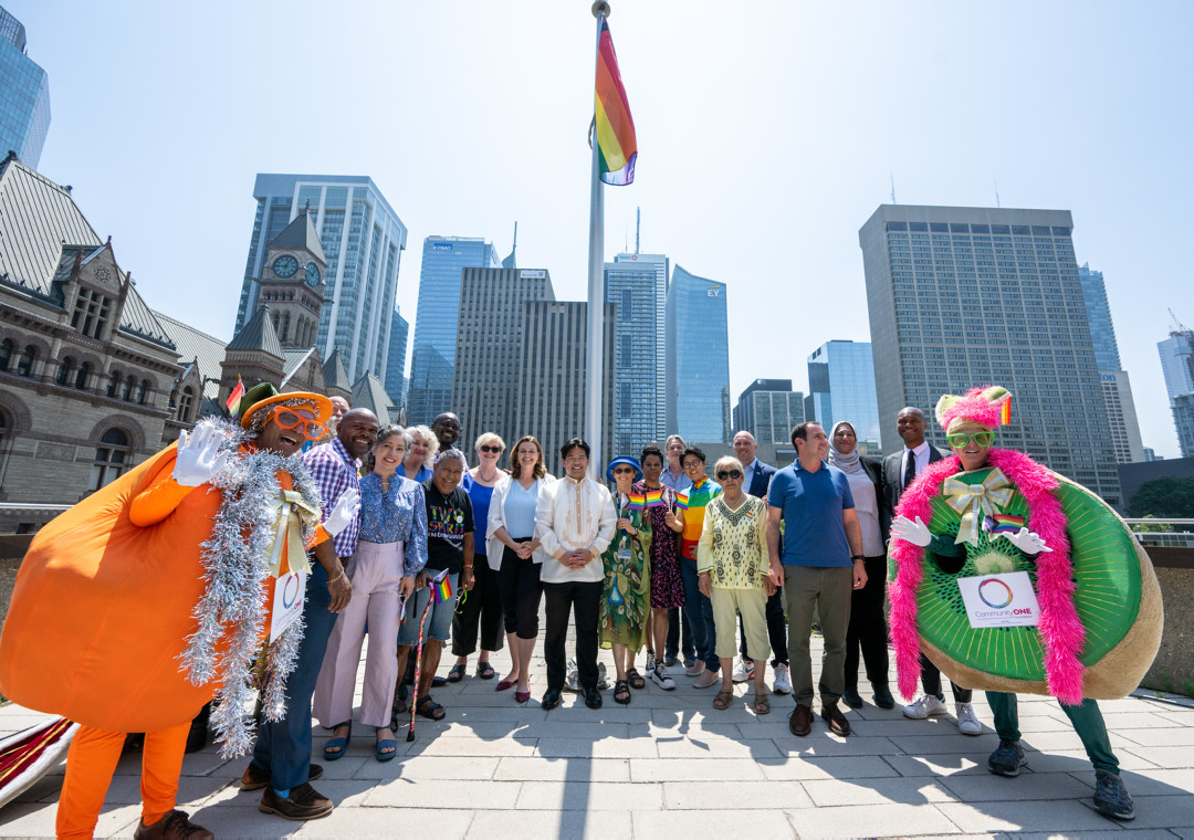 Dignitaries and guests posing for a photo with the Progress Pride Flag raised at Toronto City Hall