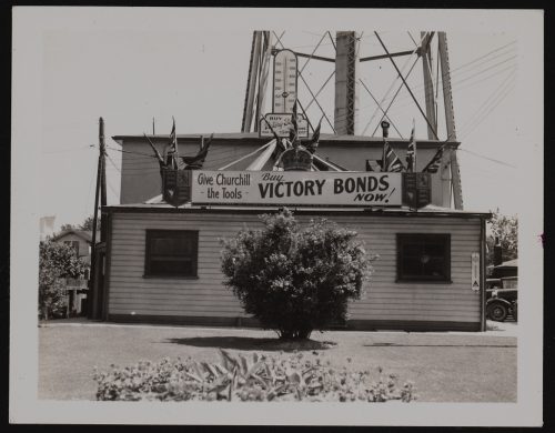 Image depicts monochrome photograph of municipal building, with base of water tower in background