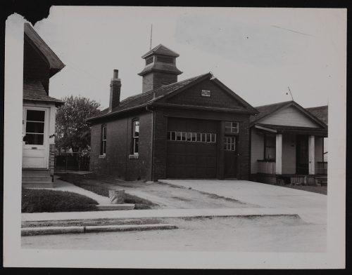 Image depicts monochrome photograph of fire station