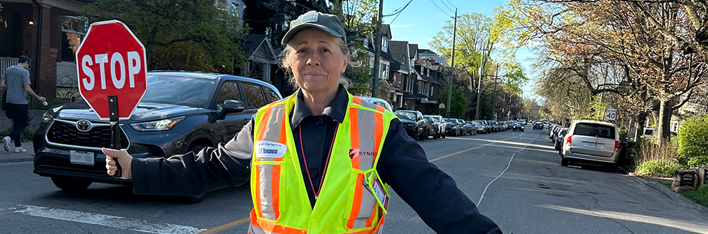 An image of a School Crossing Guard holding a red stop sign in the middle of the street.