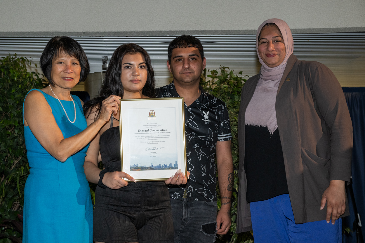 A woman and man smiling for the camera with Mayor Olivia Chow and Deputy Mayor Ausma Malik holding up a framed award.