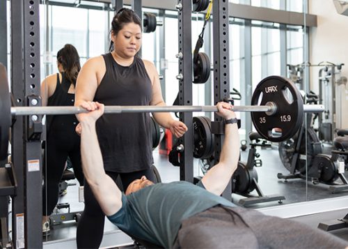 A trainer spotting a person doing a bench press in the gym.