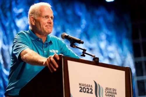 Doug Hamilton on stage talking into microphone wearing a blue shirt