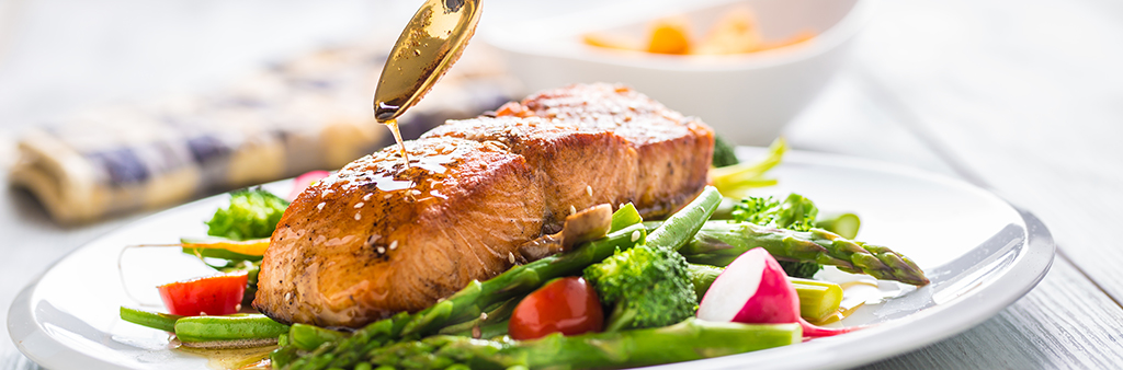 Spoon dripping sauce onto plate of salmon and vegetables