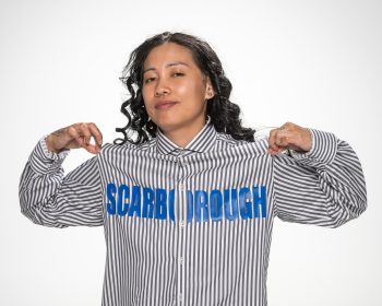 Woman posing for the camera holding up the corners of her shirt that reads Scarborough.