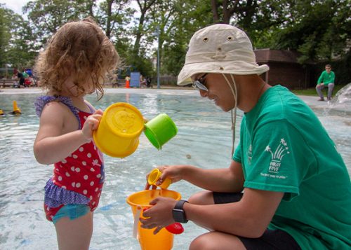 A City staff member is playing with a little girl at the wading pool.