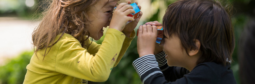 Two little children are smiling happily as they use a paper telescope to look at each other.