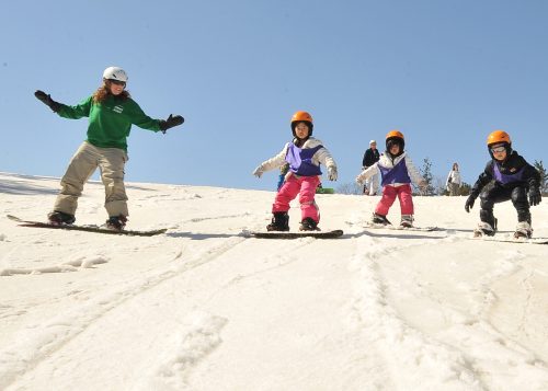 A instructor is coaching children in snowboarding at a ski hill.