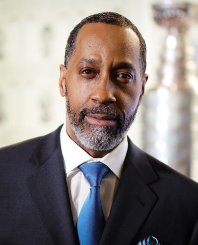 Portrait Kirk Brooks in a Black Suit, white shirt and blue tie.