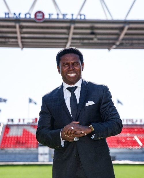 Michael ‘Pinball’ Clemons posing with hands clasps in a black suit at the BMO field. 