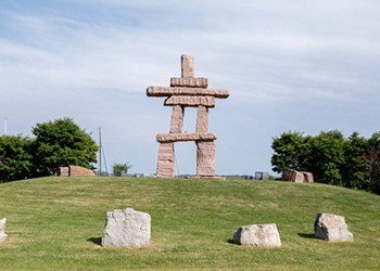 An inukshuk on top of a green hill, surrounded by other rocks and trees.