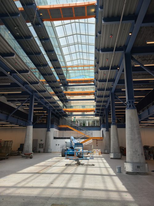 Interior of a building with pillars, a blue crane on the floor and a long skylight window above.