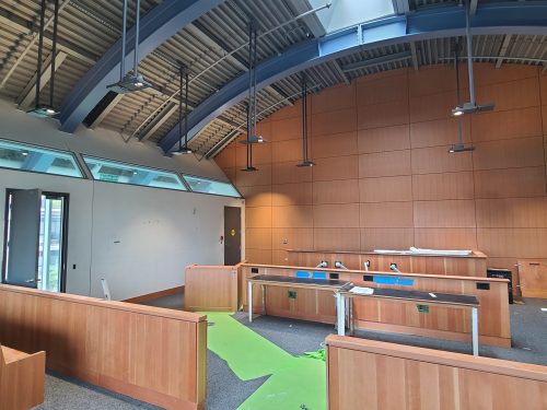 An interior with a curved ceiling, wood paneled walls and wooden spectator seating. 