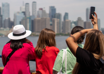 A group of women all wearing short-sleeved tops with one wearing a white hat and another taking a photo of the Toronto skyline in summer.