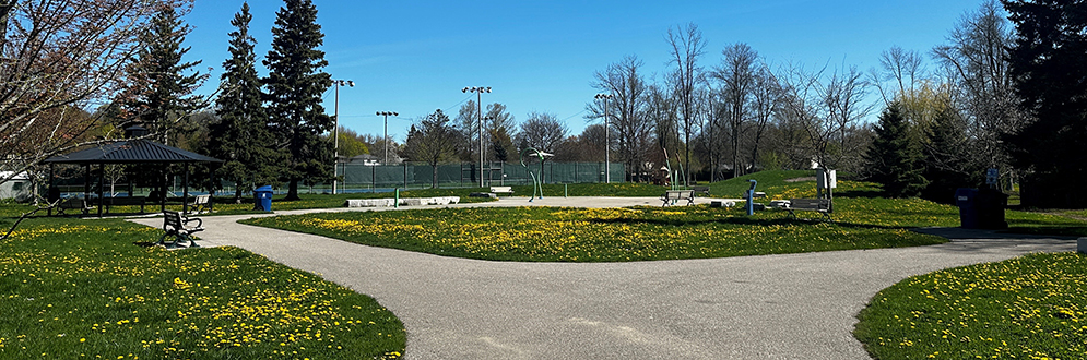 Elizabeth Simcoe Park with a pathway, gazebo, benches, trees, and a tennis court under a clear blue sky.