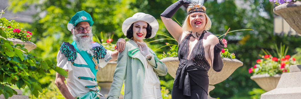 Three people wearing 1920s costumes pose outside in a garden