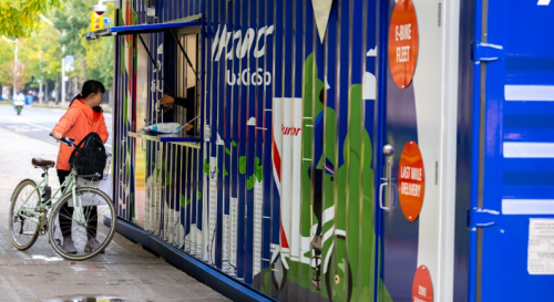 Pedestrian delivering a package to the Mini Hub through the sidewalk service window 
