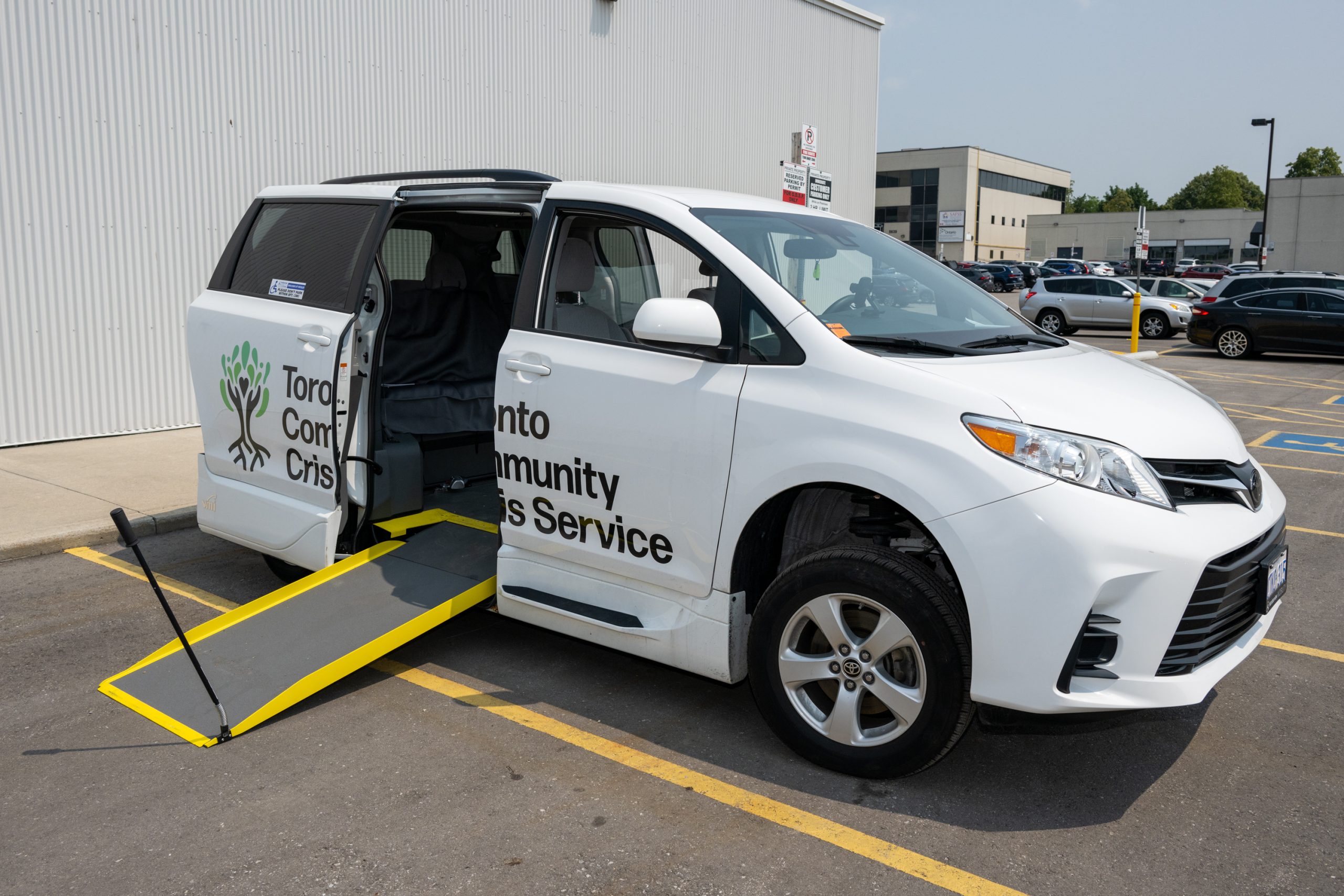 A white van with an accessibility ramp leading in the open door. The logo on the side of the vehicle reads Toronto Community Crisis Service.