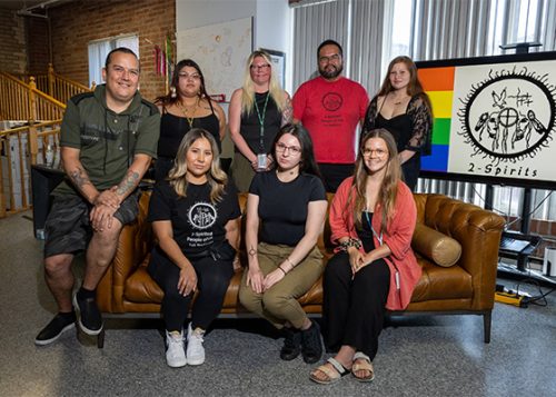A group of people posed for a photo next to a logo that reads 2-Spirits.