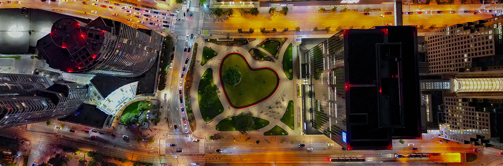An overhead aerial view of a heart shaped pond in a park surrounded by skyscrapers at night.