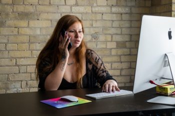 A woman sitting at a computer typing and on the phone.