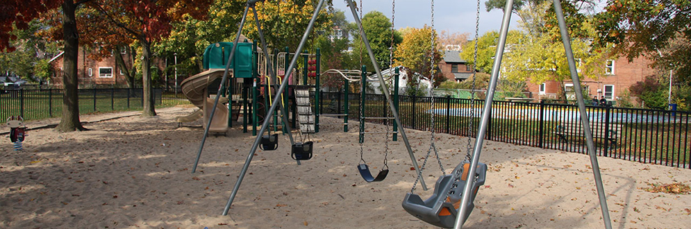 A swing set with an accessible swing, belt swing and two toddler swings. A play structure is in the background.