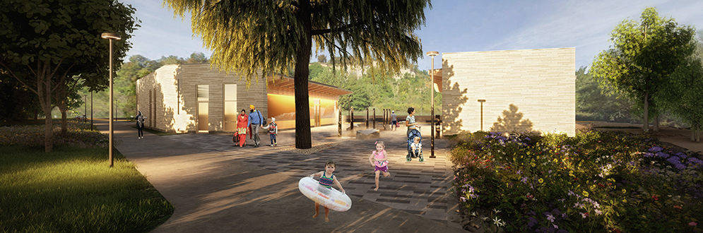 A landscaped park area featuring a modern washroom building with beige brick walls, surrounded by trees and greenery. Families and children are walking and playing in the park, with some children carrying water toys, suggesting a beach or water area nearby. Lighting and pathways lead to the building, with natural landscaping and flowers visible in the foreground.