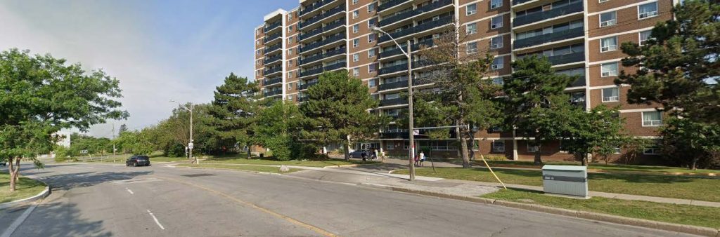 Street-level view of York Gate Boulevard showing vehicle travel lanes, a sidewalk, and residential buildings in the background