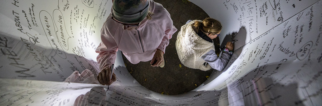 Two people seen from above draw and write on a curved wall