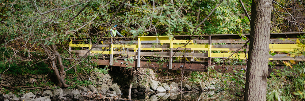 A wooden bridge with painted yellow stripes. It crosses a river.