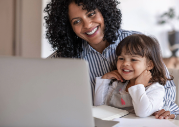 A mother and a child sitting in front of a laptop screen smiling.